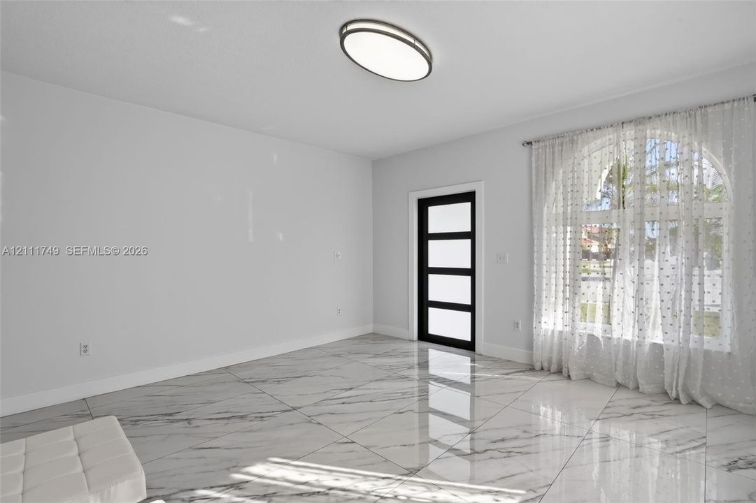 Large-format tile flooring with marble-style veining, arched window, modern door with four horizontal glass panels, and flush-mount elliptical ceiling lighting