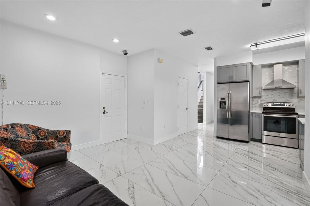 Large-format polished tile flooring, stainless steel kitchen appliances, grey shaker-style cabinetry, mosaic tile backsplash, and recessed ceiling lighting