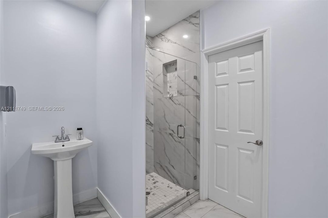 Pedestal sink with polished chrome faucet, glass-enclosed shower featuring stone-patterned tile walls, integrated shower niche, and six-panel interior door