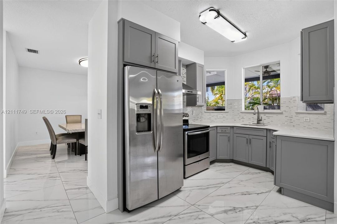Kitchen featuring gray shaker-style cabinetry, stainless steel appliances, white solid-surface countertops, mosaic tile backsplash, and polished stone-finish floor tile