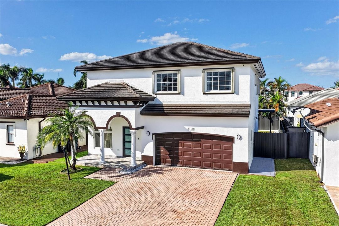 Two-story residence featuring a white stucco exterior, multi-hipped tile roof, paver driveway, two-car garage, and a covered front entry with arched accents and columns