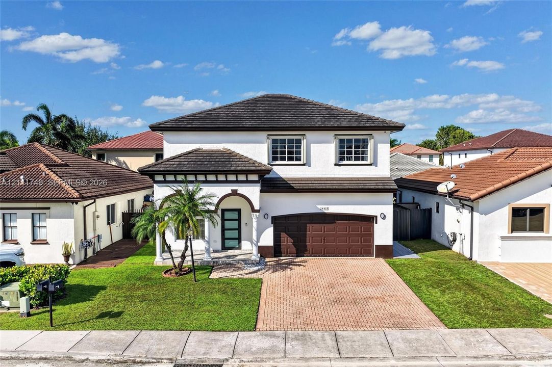 Two-story stucco exterior featuring a multi-hipped tile roof, paver driveway, covered entryway with arched architectural detailing, and a multi-panel garage door