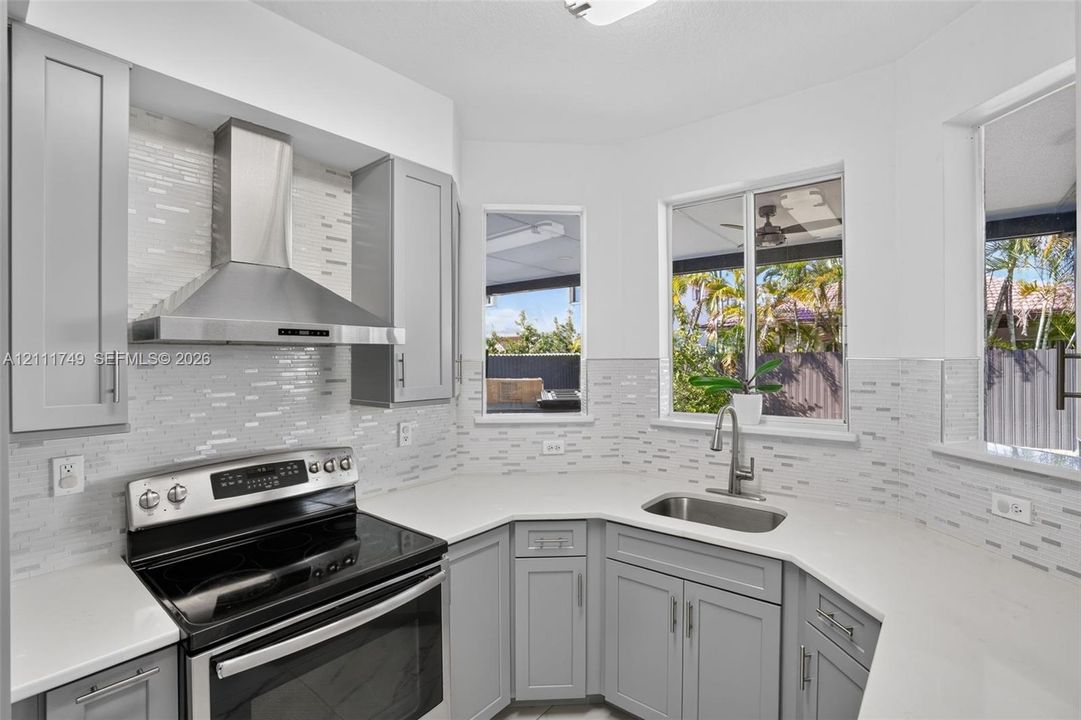 Kitchen featuring grey shaker-style cabinetry, quartz countertops, a stainless steel range with a matching chimney-style hood, and a decorative tile backsplash