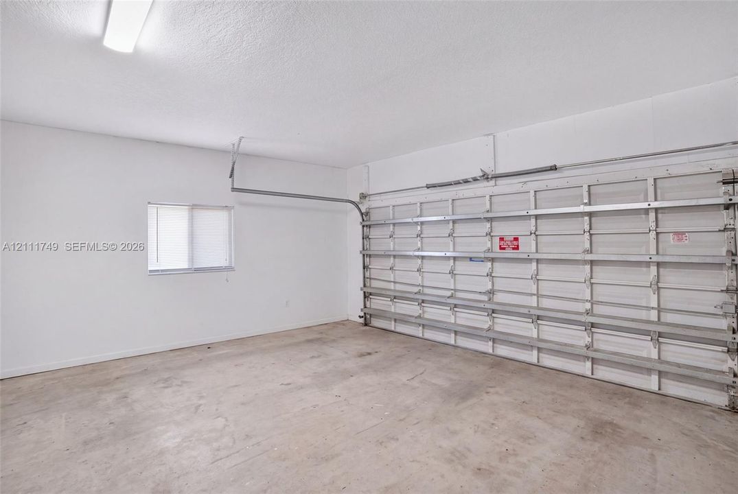 Two-car garage featuring a concrete floor, painted walls, single sliding window, and a metal roll-up door