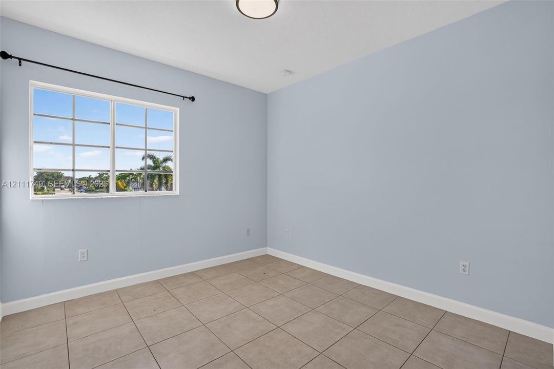 Neutral-toned interior space featuring light-colored tile flooring, smooth walls, a multi-pane window with a black curtain rod, and a central flush-mount ceiling light