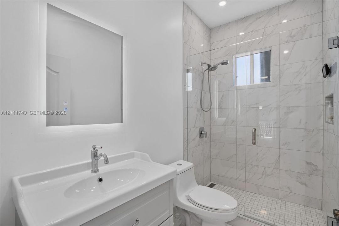 Bathroom featuring a vanity with an integrated sink, backlit wall-mounted mirror, walk-in shower with a glass enclosure, and stone-patterned wall tile