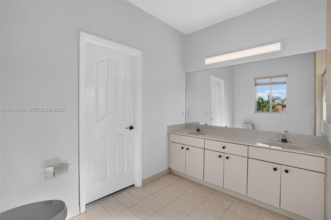 Dual-sink vanity with a wide countertop, large wall-mounted mirror, linear light fixture, and tile flooring