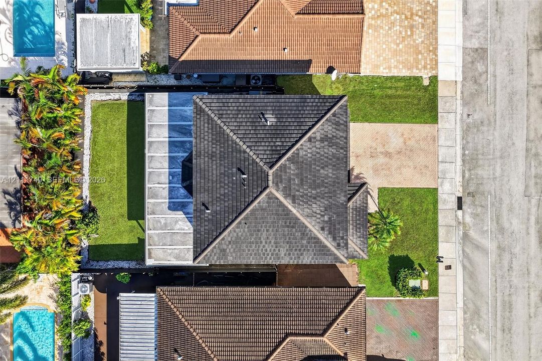 Aerial perspective showcasing a hip roof structure, paved driveway, landscaped lawn area, and concrete patio covering