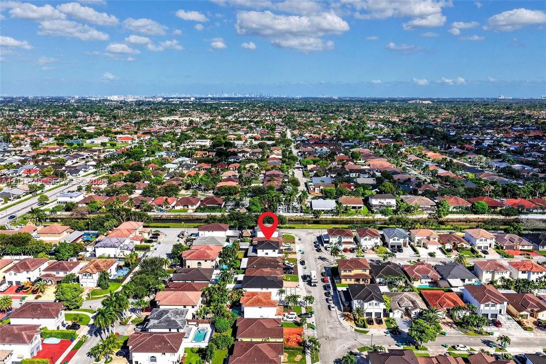 Aerial perspective of a residential property featuring a multi-story residence with a pitched roof, situated within an established suburban neighborhood with mature trees and a nearby waterway