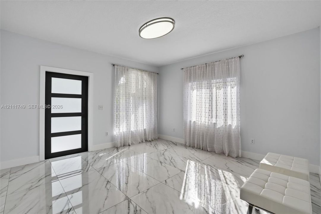 Large-format stone-patterned tile flooring, four-panel black door with frosted glass inserts, and a modern oval flush-mount ceiling fixture
