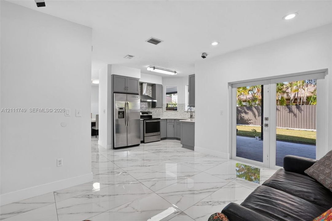 Kitchen featuring grey cabinetry, stainless steel appliances, tiled backsplash, large-format tile flooring, and double-glass doors