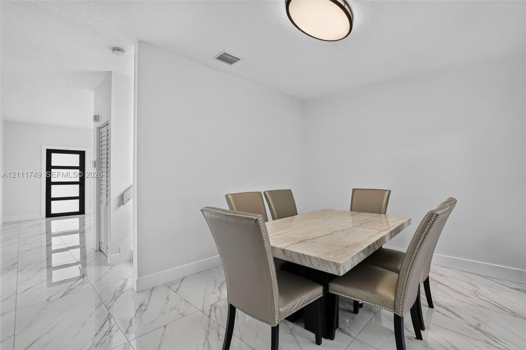 Large-format white tile flooring with grey veining, flush-mount circular ceiling fixture, and multi-panel exterior door with glass inserts