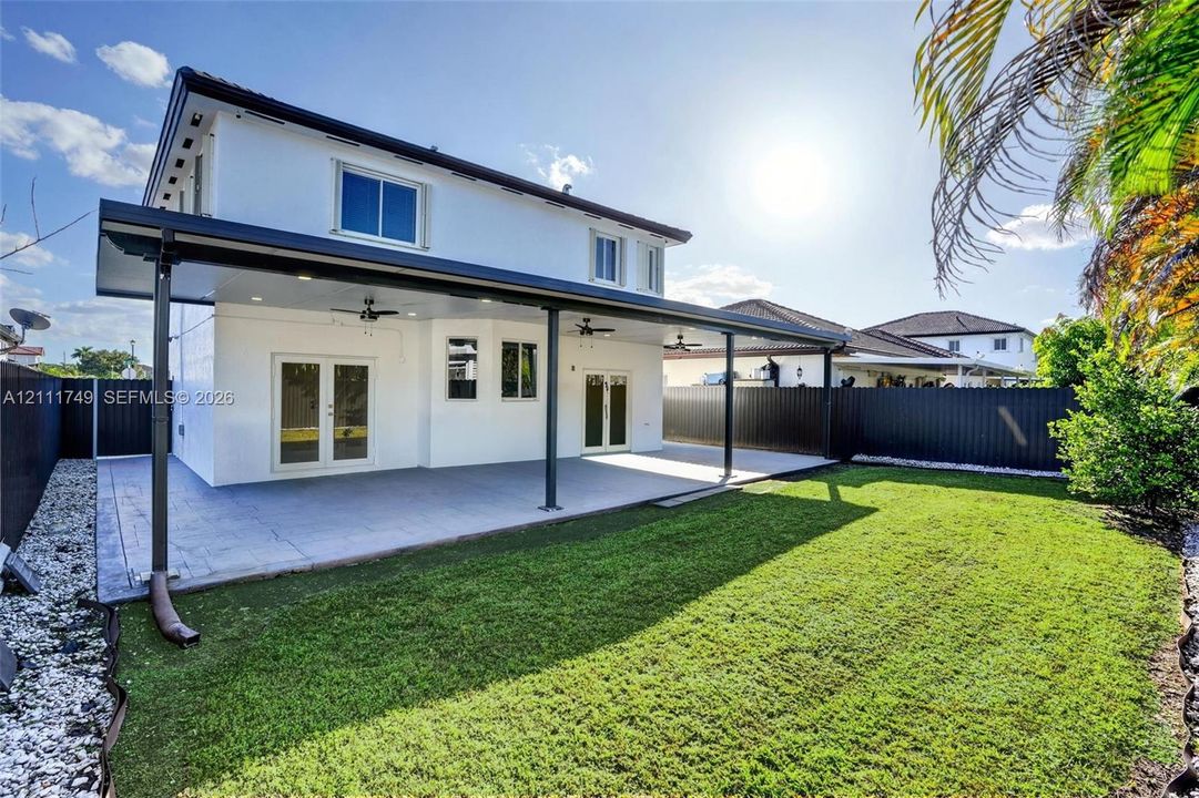 Covered rear patio with recessed lighting and ceiling fans, tiled flooring, white stucco exterior, and fenced backyard with manicured lawn