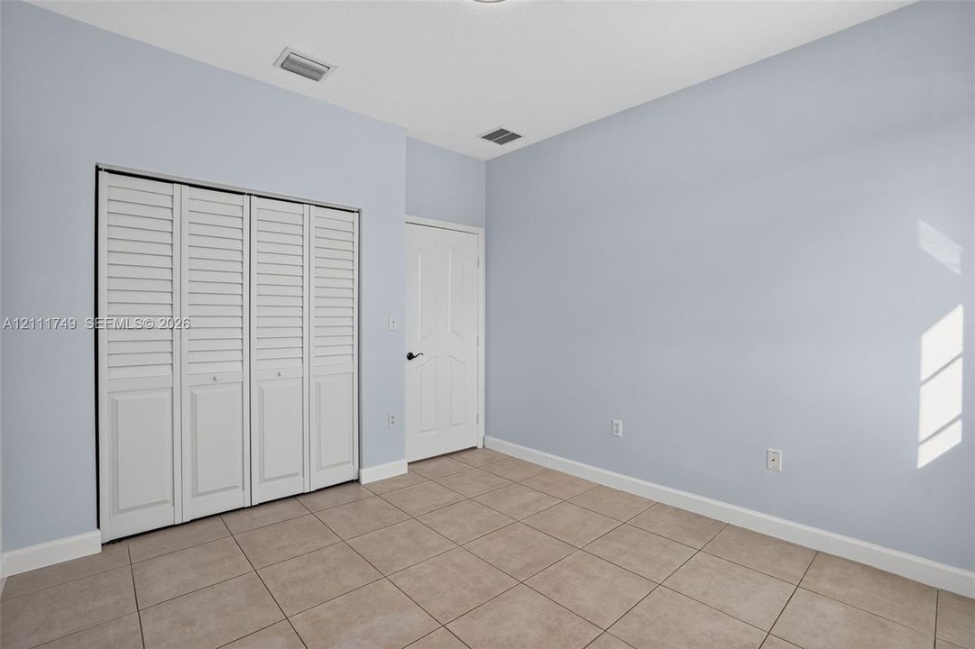 Neutral-toned interior space featuring light-colored ceramic tile flooring, four-panel louvered closet doors, and a solid-core door with matte black hardware