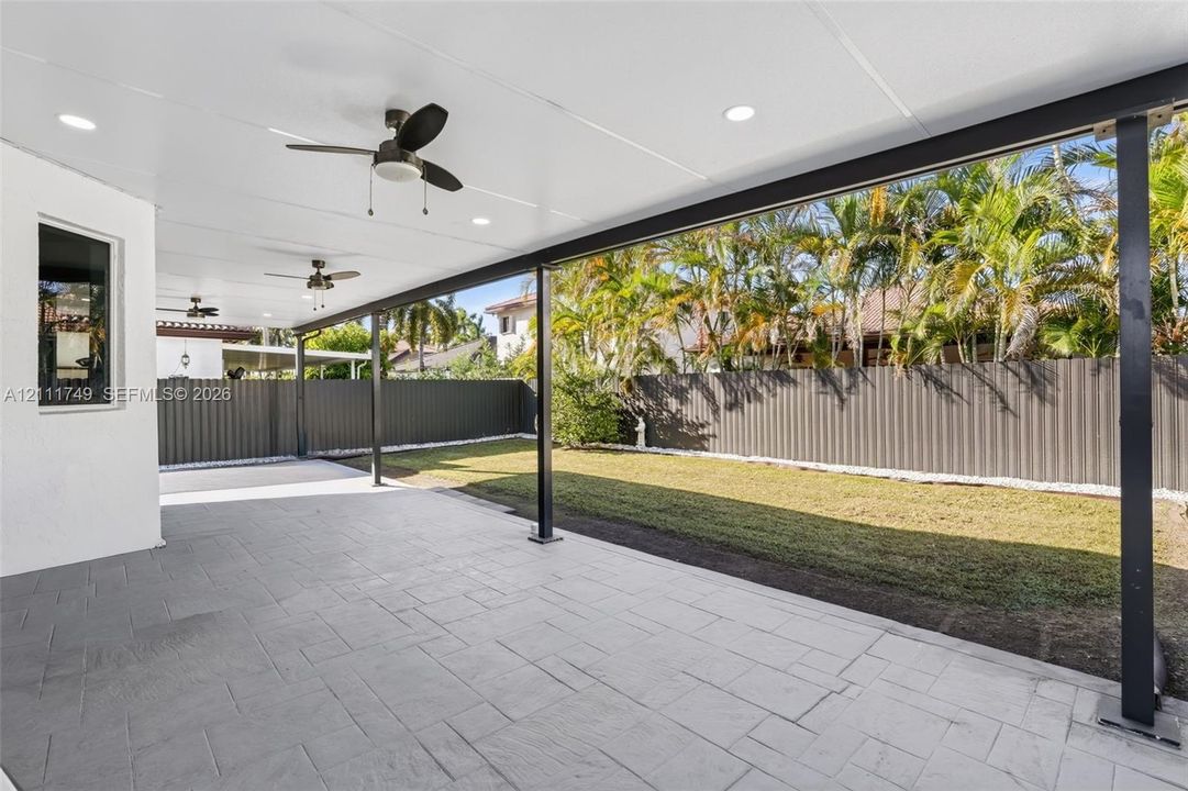 Covered concrete patio featuring recessed lighting, dual ceiling fans, metal support columns, and a fenced backyard with lawn space