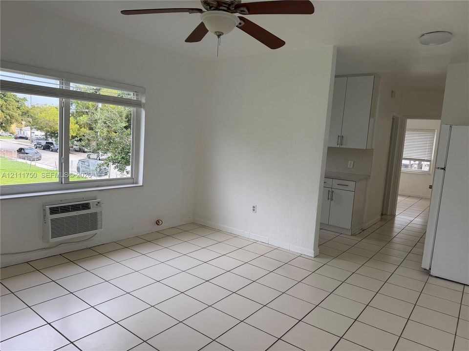 Large-format ceramic tile flooring, neutral wall finishes, integrated wall-mounted cooling unit, and overhead ceiling fan