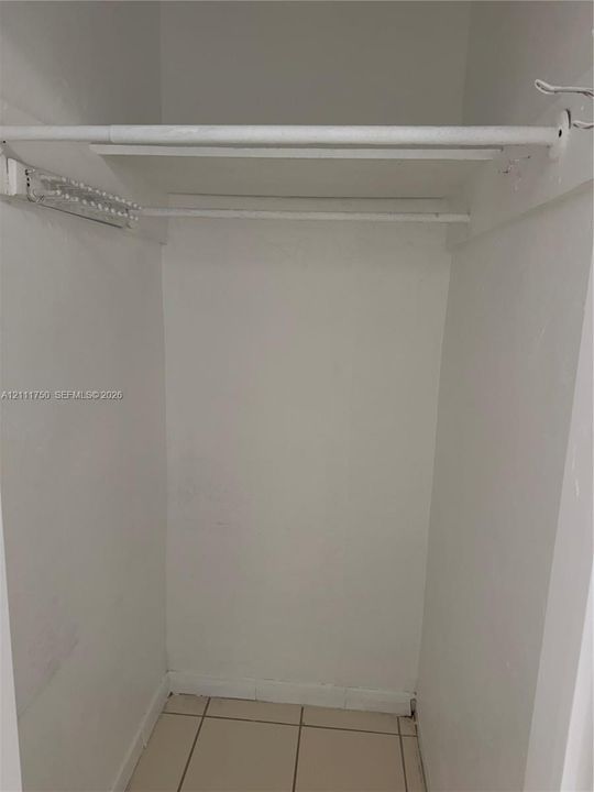 Storage closet featuring tiled flooring, a built-in overhead shelf, and a painted metal rod