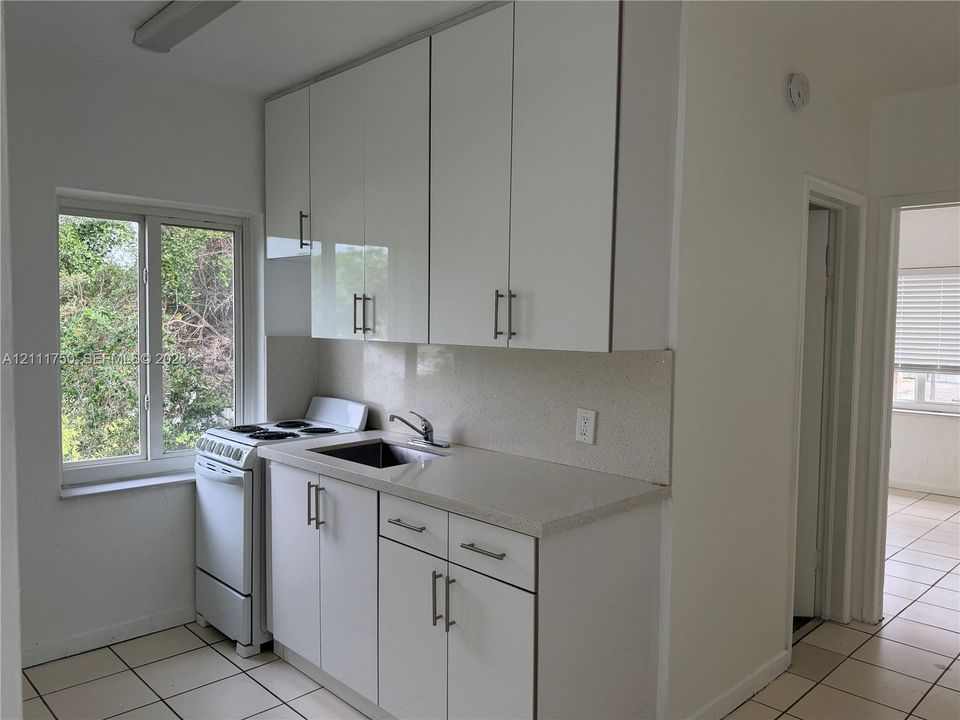 Kitchen featuring white high-gloss cabinetry, stone-finish countertops, stainless steel sink, tile flooring, and oversized window
