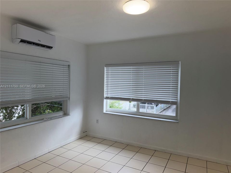 Interior space featuring tile flooring, neutral walls, two horizontal windows with fitted blinds, and a wall-mounted ductless air conditioning unit