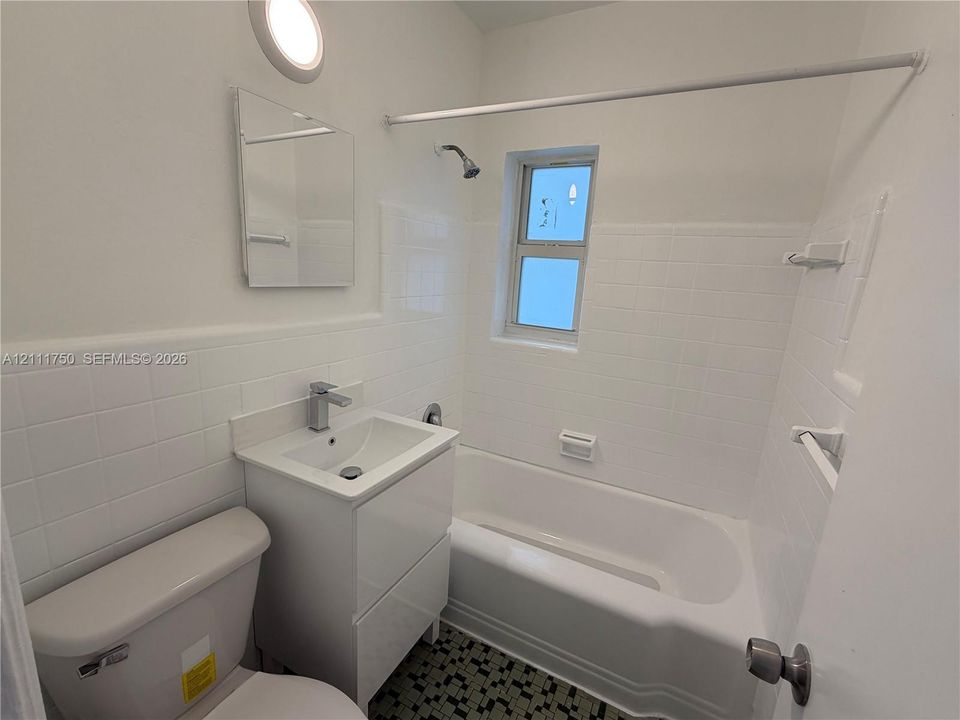 Bathroom featuring a white vanity cabinet, square basin with a chrome faucet, bathtub-shower combination with white wall tile, and patterned tile flooring