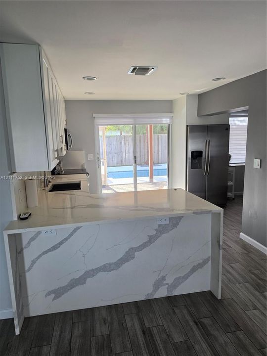 Kitchen featuring a waterfall-edge stone countertop, white shaker-style cabinetry, stainless steel refrigerator, recessed lighting, and wood-finish flooring