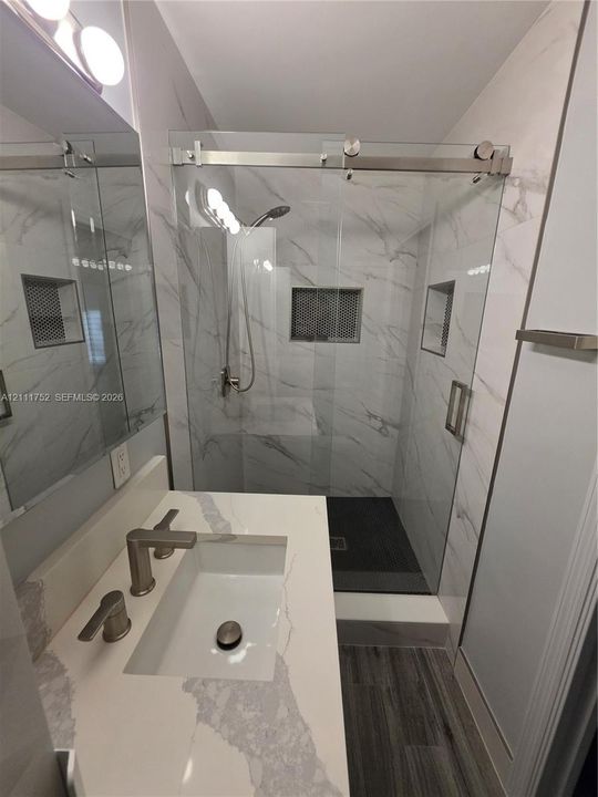 Bathroom featuring a vanity with a stone-finish countertop, walk-in shower with sliding glass doors, floor-to-ceiling tile work, and recessed wall niches