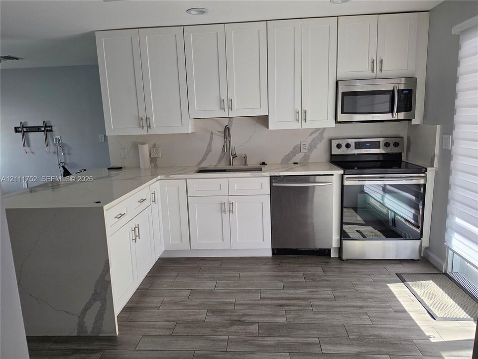 Kitchen featuring white shaker-style cabinetry, quartz countertops with a waterfall edge, stainless steel appliances, and wood-finish tile flooring