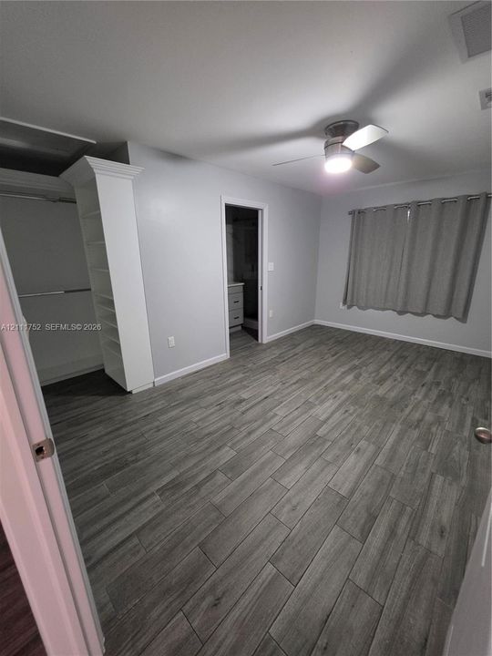 Wood-finish tile flooring, ceiling fan with integrated lighting, built-in shelving, and neutral wall tones