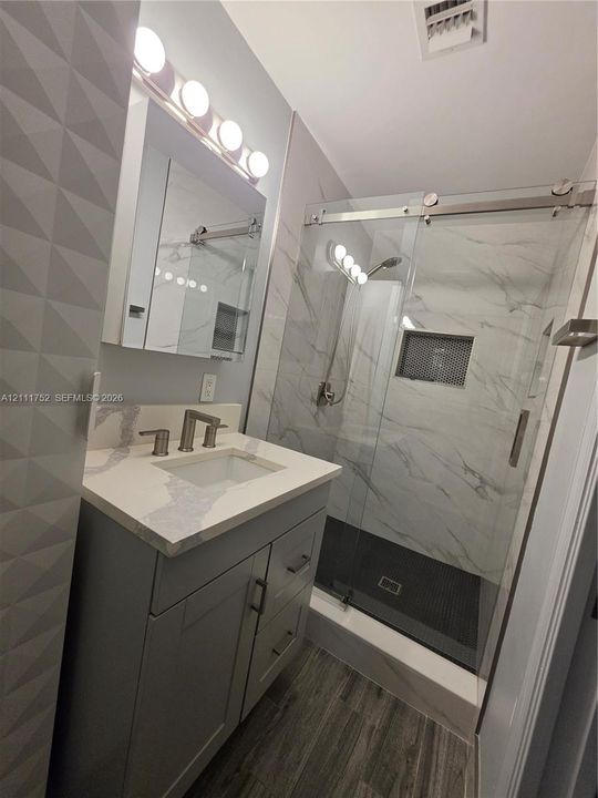 Bathroom featuring a vanity with a quartz countertop and integrated sink, a glass-enclosed shower with tiled walls and built-in niche, and wood-finish flooring