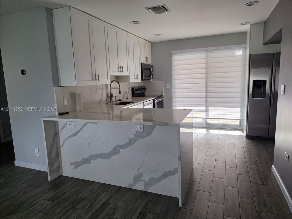 Kitchen featuring white cabinetry, stone-patterned waterfall countertop, stainless steel appliances, and wood-finish flooring