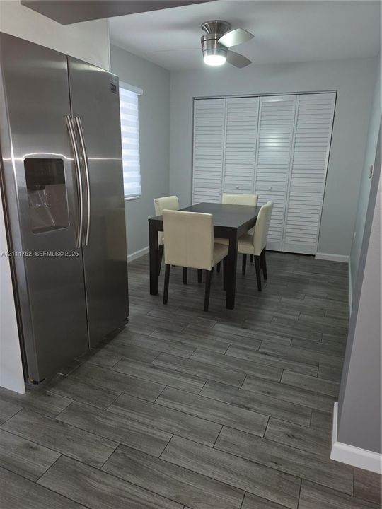 Wood-finish flooring, stainless steel side-by-side refrigerator, ceiling-mounted light fixture, and floor-to-ceiling louvered closet doors