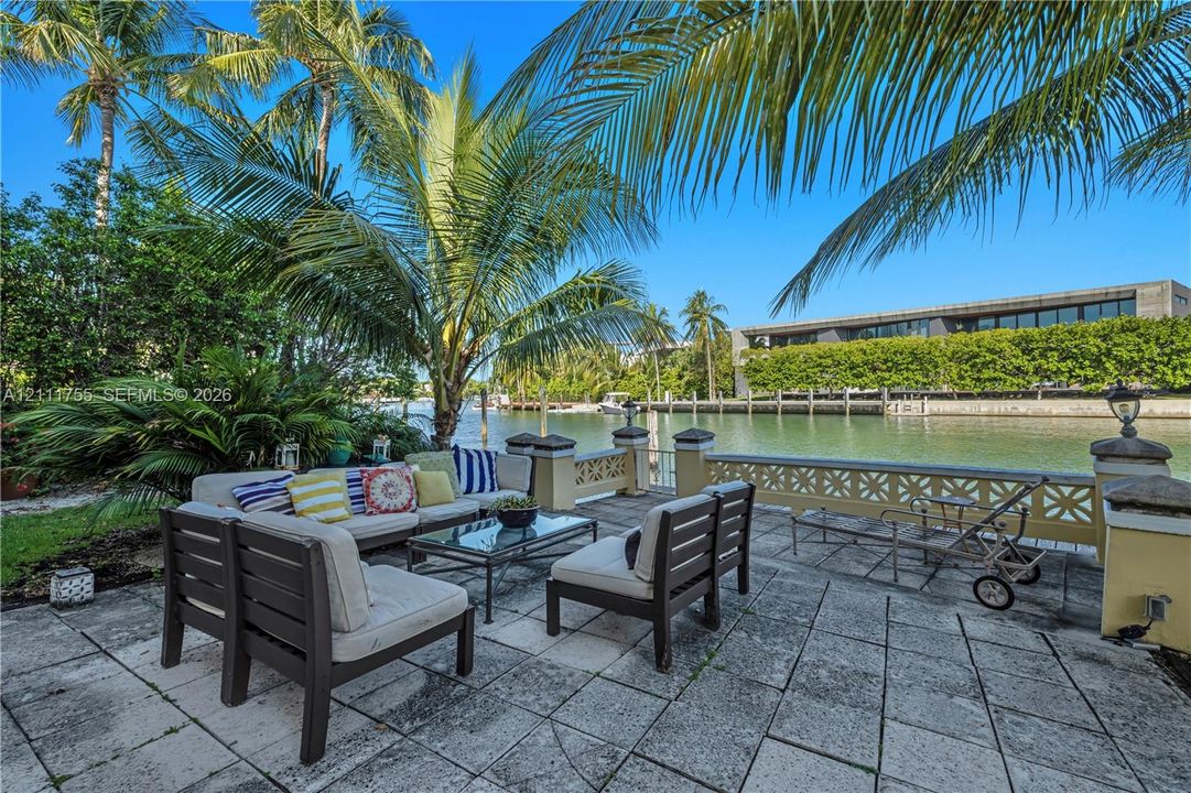 Waterfront patio featuring stone pavers, decorative masonry perimeter wall, mature palm trees, and direct bulkhead access