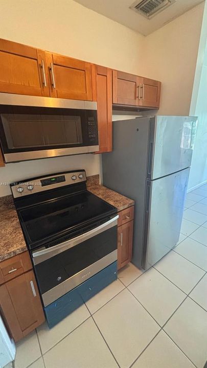 Kitchen featuring wood-finish cabinetry, stone-patterned countertops, stainless steel appliances, and tile flooring