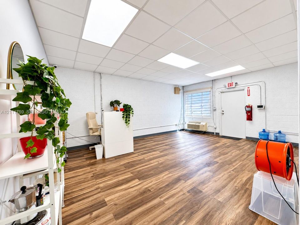 Open-concept space featuring wood-finish flooring, painted masonry walls, recessed panel ceiling, and a wall-mounted climate control unit