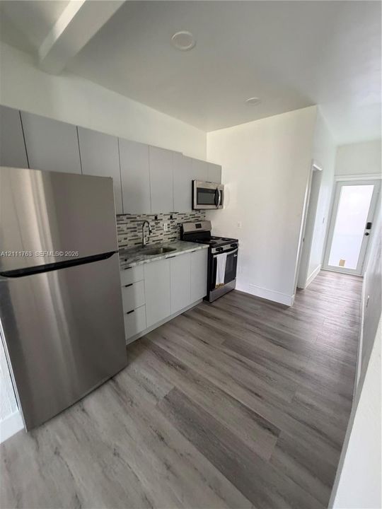 Kitchen featuring flat-panel cabinetry, stone-finish countertops, stainless steel appliances, decorative tile backsplash, and wood-finish flooring