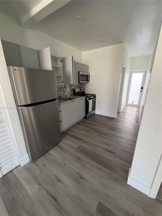 Kitchen featuring wood-finish flooring, stainless steel appliances, flat-panel cabinetry, a multi-tonal tile backsplash, and recessed lighting