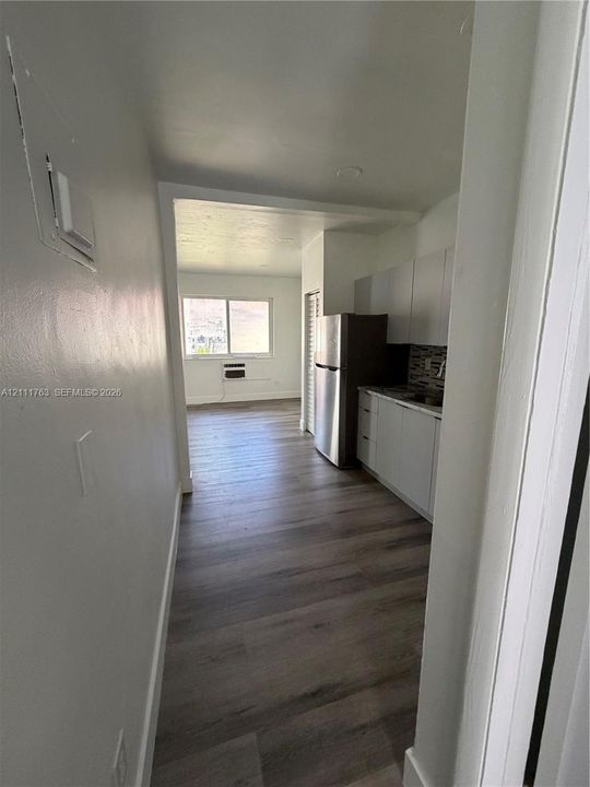 Kitchen featuring white cabinetry, wood-finish flooring, a stainless steel refrigerator, and a tiled backsplash