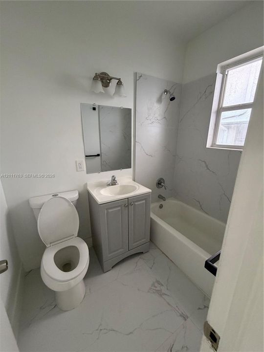 Bathroom featuring a vanity with a white composite countertop, large-format stone-patterned tile flooring, full-height stone-patterned tile shower surround, and a wall-mounted light fixture