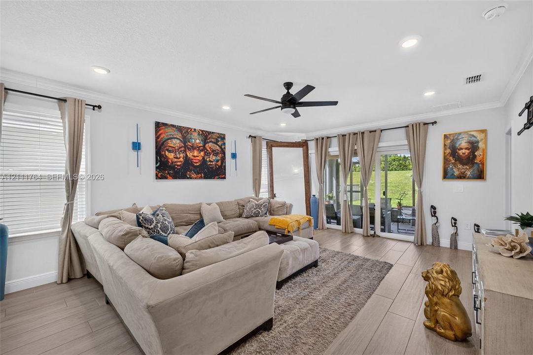 Living area featuring wood-finish tile flooring, recessed lighting, crown molding, and a central ceiling fan, with sliding glass doors providing outdoor access