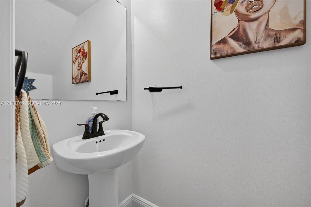 Wall-mounted pedestal sink featuring a curved basin and matte black faucet, paired with a large frameless mirror and matching matte black hardware