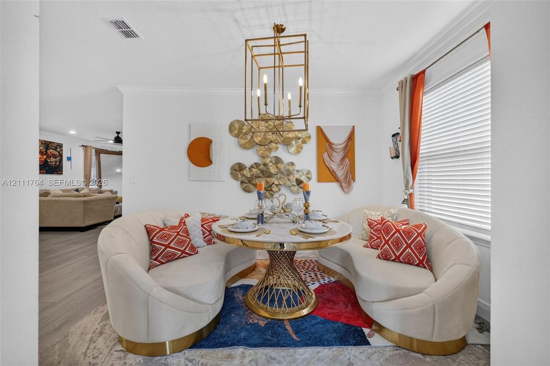 Geometric gold-tone pendant light fixture featuring six candelabra-style bulbs, multi-panel window with horizontal blinds, and wood-finish flooring