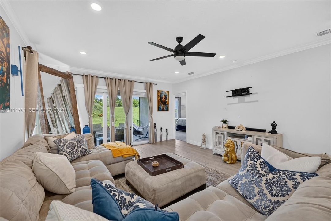 Living area featuring wood-finish flooring, recessed lighting, crown molding, a ceiling fan, and sliding glass doors