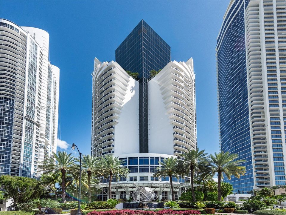 High-rise residential tower featuring a white concrete facade, glass-paneled curtain walls, and stacked curvilinear balconies