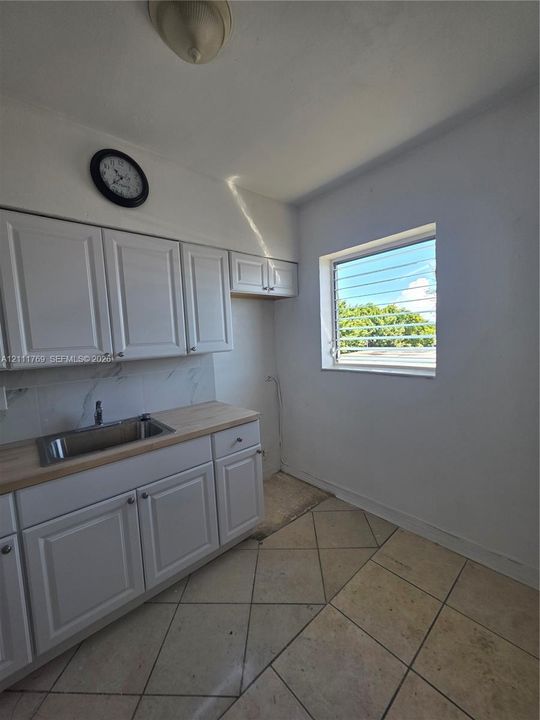 White shaker-style cabinetry, stainless steel sink, wood-finish countertop, tiled backsplash, and diagonal tile flooring