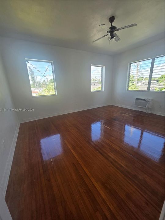 Room featuring wood-finish flooring, white walls, multiple louvered windows, and a ceiling fan