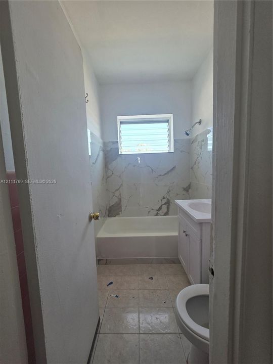 Bathroom featuring a combination bathtub and shower with large-format decorative tile surround, white cabinetry vanity with integrated sink, and louvered window