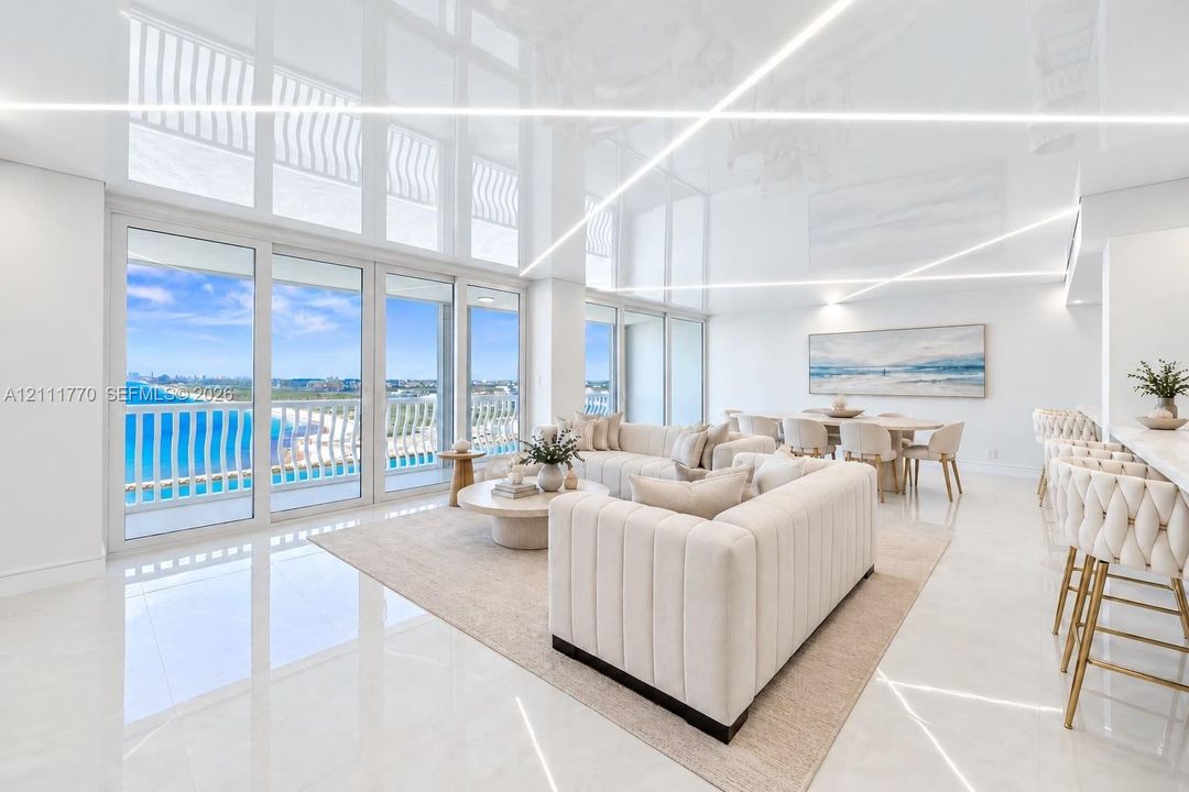 High-gloss ceiling with integrated linear lighting, large-format tile flooring, and expansive floor-to-ceiling glass sliding doors opening to a balcony with an ocean backdrop