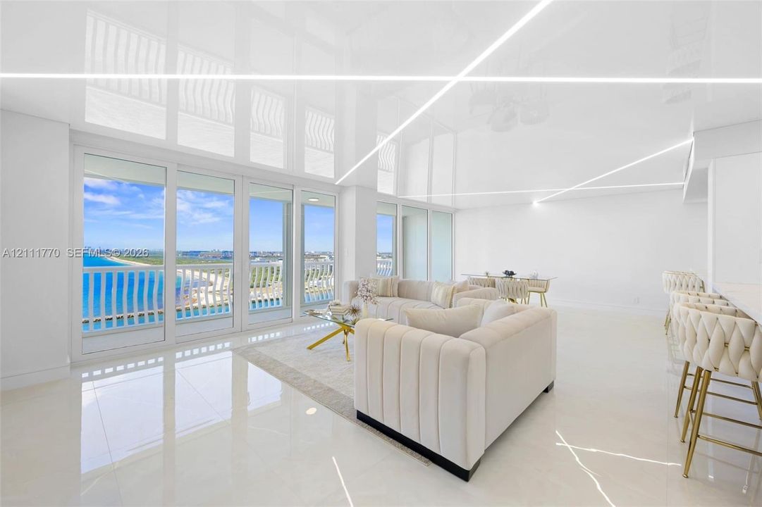 Open-concept space featuring high-gloss ceilings with recessed linear lighting, polished tile flooring, and floor-to-ceiling sliding glass doors opening to a balcony with coastal scenery