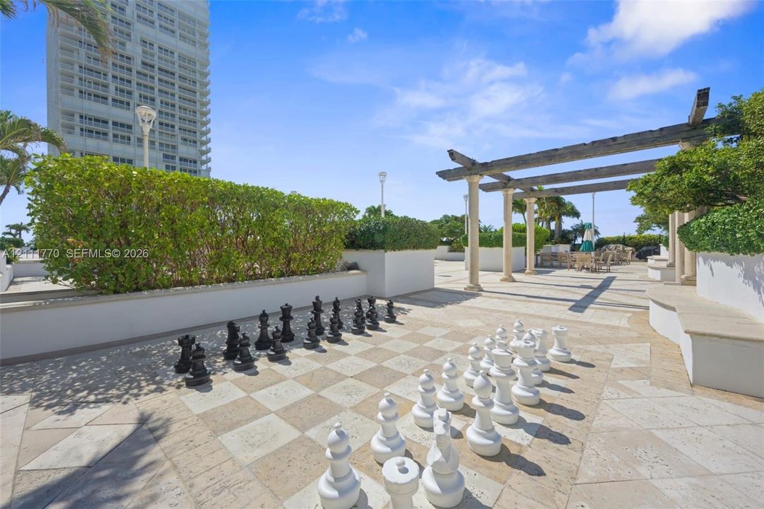 Outdoor terrace featuring stone tile flooring, a built-in pergola, custom raised planter boxes with manicured hedges, and a permanent oversized chess set