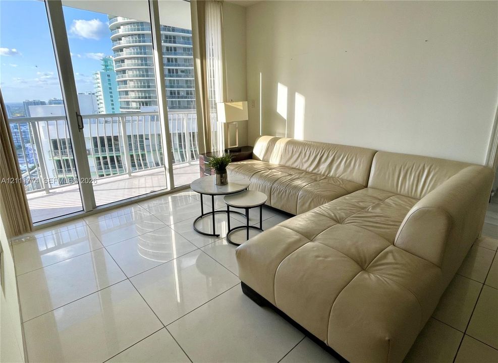Floor-to-ceiling glass sliding doors, large-format tile flooring, and an integrated balcony with metal railings
